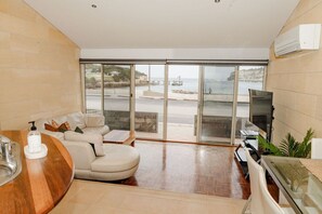 A modern living room with a sofa, a coffee table, a TV, and a view of the sea through large glass doors.