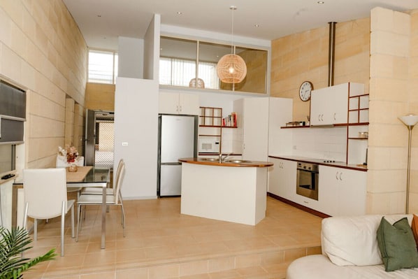 A modern kitchen with a central island, a dining area with chairs, and a living space with a sofa.