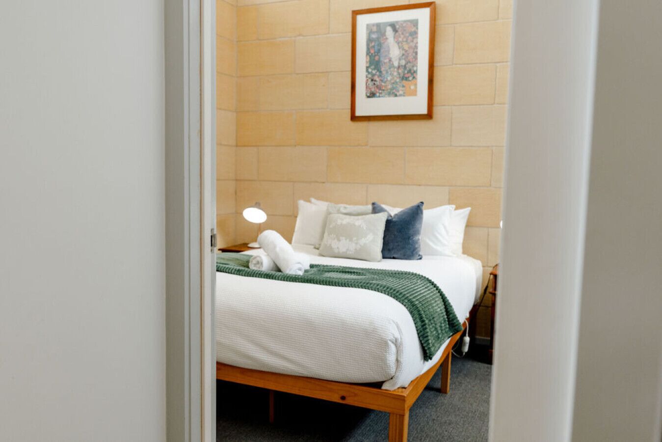 A hotel room with a bed, pillows, a blanket, a bedside lamp, and a framed picture on the wall.