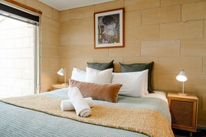 A hotel room with a large bed, a headboard, two bedside tables with lamps, a framed picture on the wall, and a window.