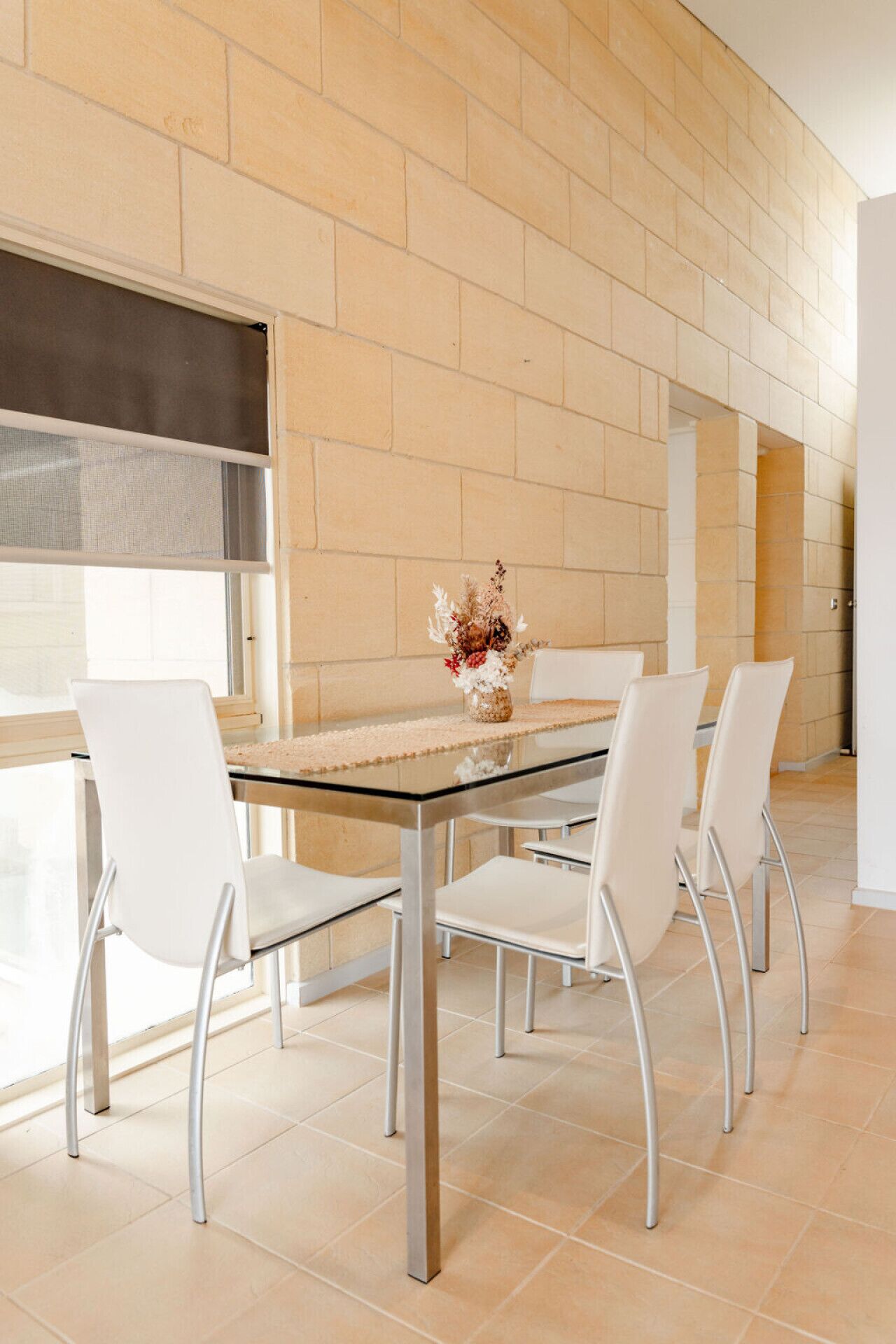 Un espace repas moderne avec une table en verre, des chaises blanches et un vase rempli de fleurs séchées.