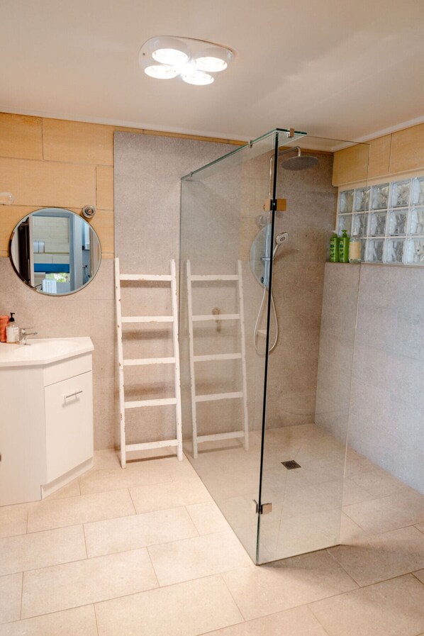 A modern bathroom with a glass-enclosed shower, a white vanity, a mirror, and a tiled floor.