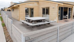 A single-story building with a flat roof, a patio area with a table and benches, and a sliding glass door entrance.
