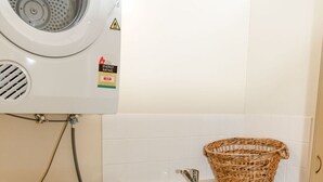 A compact laundry area with a washing machine, a dryer, and a sink with a basket on the countertop.