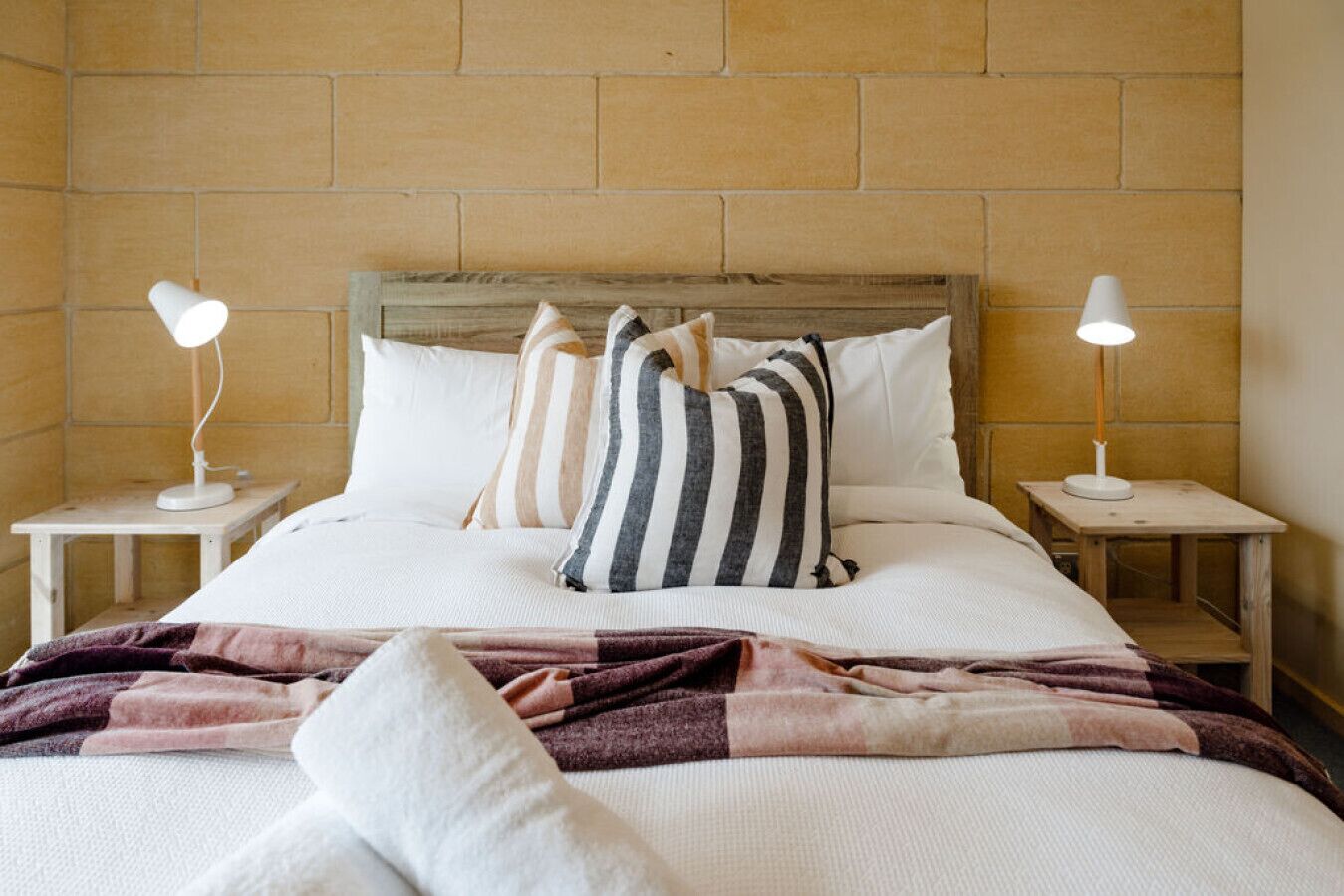 A bed with a wooden headboard, two bedside lamps, and striped pillows.