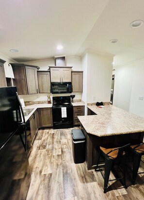 A modern kitchen with a central island, wooden cabinets, and a black stove.