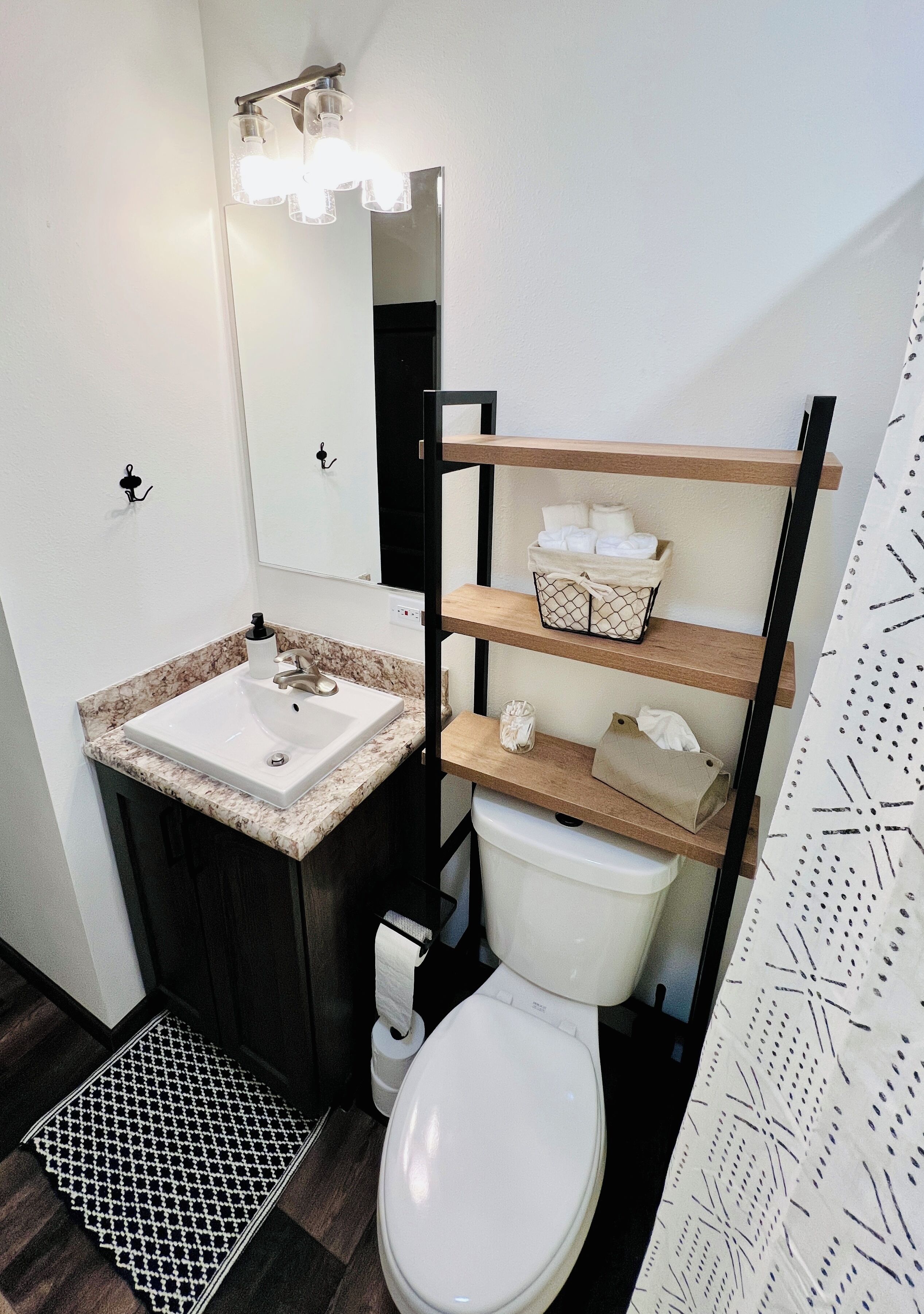 Un baño con un lavamanos blanco, un inodoro, un espejo y una estantería con toallas.