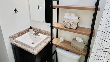 Un baño con un lavamanos blanco, un inodoro, un espejo y una estantería con toallas.