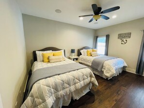 Ein Schlafzimmer mit zwei Betten, einem Deckenventilator, einem Nachttisch mit Lampe und einem Fenster mit Vorhängen.