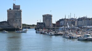 A harbor with multiple boats docked, a prominent tower, and a building with a flag. - Charmante maisonnette (La Rochelle)