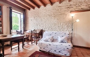 Ein Zimmer mit Steinwand, einem Holztisch mit Stühlen, einem Bett mit gemusterten Textilien und einer Stehlampe.