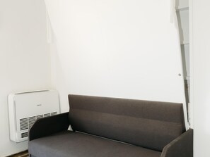 A compact room with a grey sofa, a white wall, and a white air conditioning unit. - Albariño Harbor's Light (La Vila Joiosa)