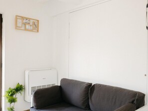 A room with a grey sofa, a white air conditioning unit, and a small plant. - Garnacha Harbor's Light (La Vila Joiosa)