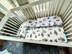 Una cuna blanca con colchón y almohadas con motivos espaciales.