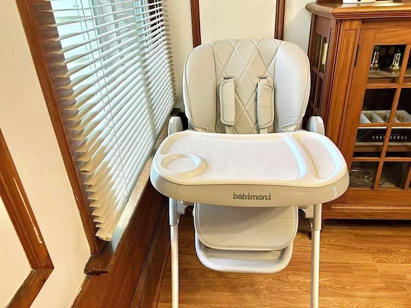 Una silla alta con bandeja, ubicada junto a una ventana con persianas.