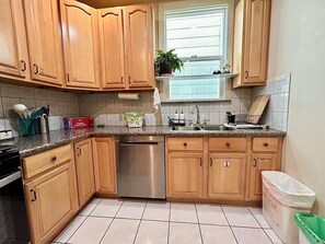 Cocina con alacenas de madera, lavavajillas de acero inoxidable, un lavatorio y una ventana sobre la encimera.