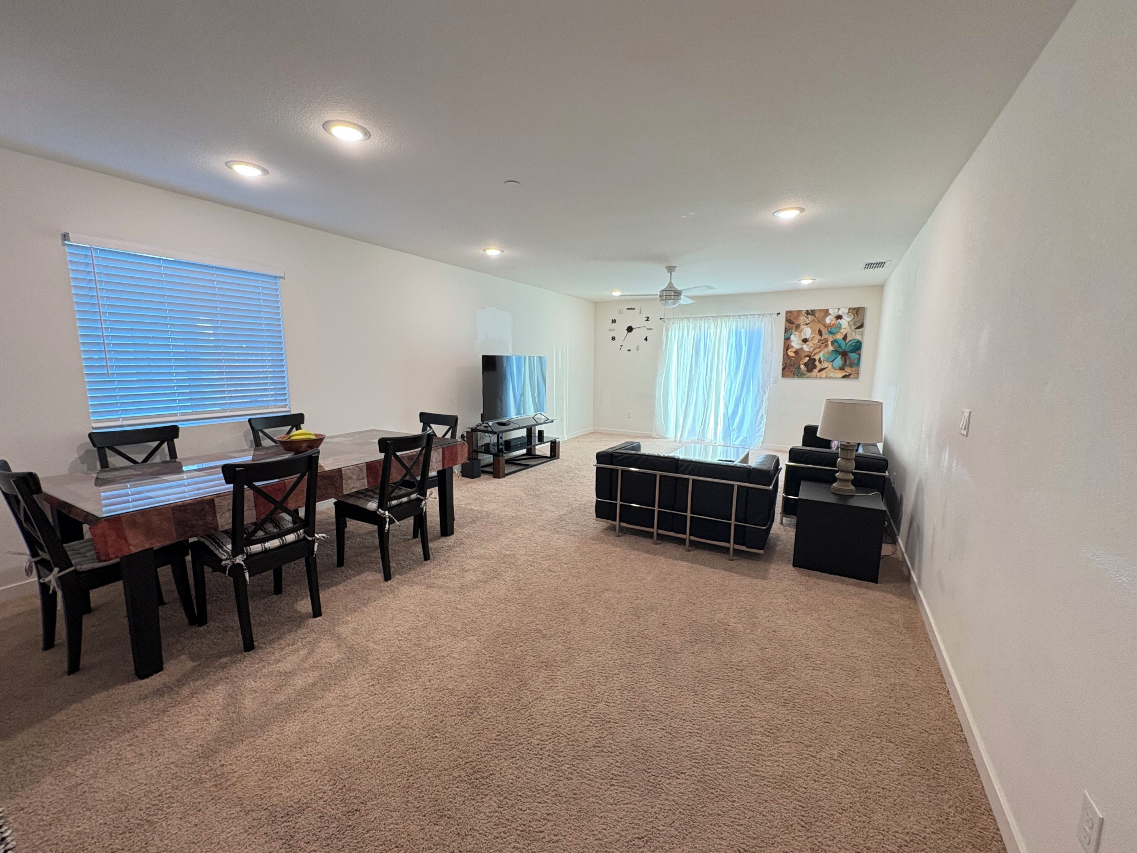 A spacious living room with a dining area, carpeted floor, and a ceiling fan.