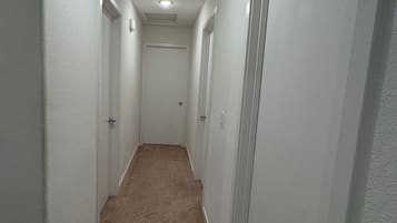 En smal hall med mattbeklädd golv och vita väggar, som leder fram till en dörr i slutet.