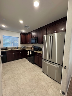 A modern kitchen with dark wood cabinets, stainless steel appliances, and a window with blinds.