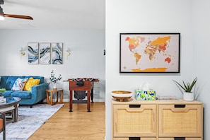 Ein Wohnzimmer mit blauem Sofa, einem Holztisch, einem kleinen Beistelltisch, einer Wandweltkarte und einer Kommode mit Korbspeicher.