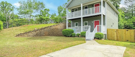 A two-story house with a front porch, a red door, and a stone retaining wall.