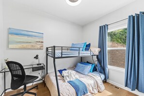 Ein Schlafraum mit Etagenbetten, Schreibtisch, Stuhl und einem Bild an der Wand.