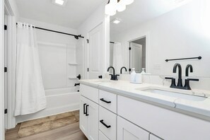 Et moderne badeværelse med et hvidt toiletbord, armatur i sort og et stort spejl.