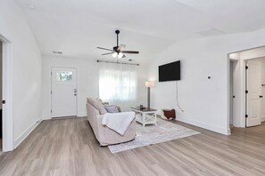 A spacious living room with a ceiling fan, a sofa, a coffee table, and a flat-screen TV mounted on the wall. - The Modern Getaway, 3BR, Workspace + Downtown Kannapolis (Kannapolis)