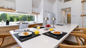 A modern kitchen with a large island, white cabinetry, and a view of greenery outside.