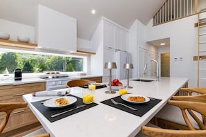 A modern kitchen with a large island, white cabinetry, and a view of greenery outside.