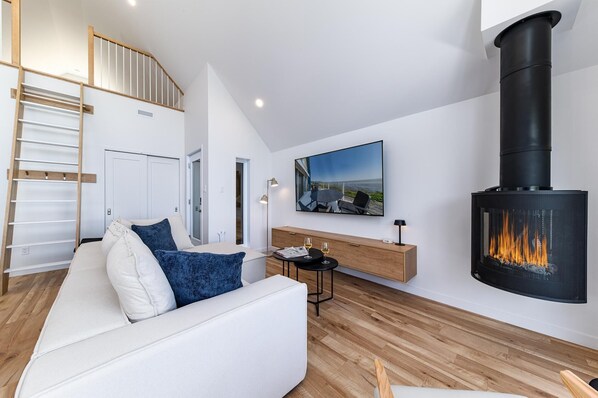 A modern living room with a white sofa, a black fireplace, and a wooden floor.