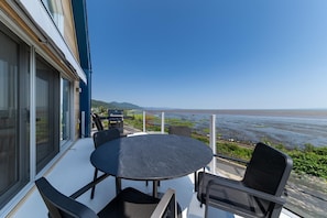 A balcony with a round table and chairs, overlooking a beach and water body. - Le Grand Bleu 1265: Waterfront with River Views (Petite-Rivière-Saint-François)