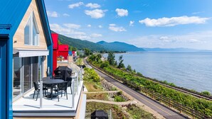A coastal property with a balcony overlooking a vineyard and a body of water.