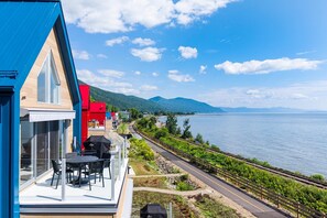 A coastal property with a balcony overlooking a vineyard and a body of water.
