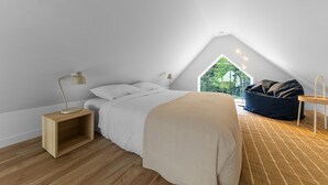 A bedroom with a bed, bedside table, lamp, and a view of greenery outside.