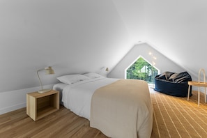 A bedroom with a bed, bedside table, lamp, and a view of greenery outside.