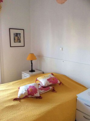 A bed with a yellow bedspread and two pillows with floral patterns, a bedside table with a lamp, and a framed picture on the wall. - Sea View Paradise Retreat in Nikiti (Nikiti)
