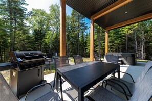 Una veranda esterna con barbecue, tavolo e sedie, immersa nel verde.