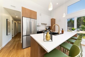 A modern kitchen with a stainless steel refrigerator, a central island with bar stools, and a view of the outdoors.