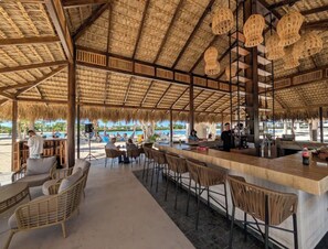 An outdoor bar area with wicker furniture, a thatched roof, and a view of the beach. - Tropical Bliss apt, Beach, Golf, Dining,Gated community near downtown Punta Cana (Punta Cana)