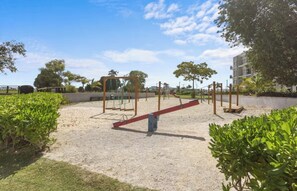 An outdoor playground with swings, a slide, and a seesaw. - Tropical Bliss apt, Beach, Golf, Dining,Gated community near downtown Punta Cana (Punta Cana)