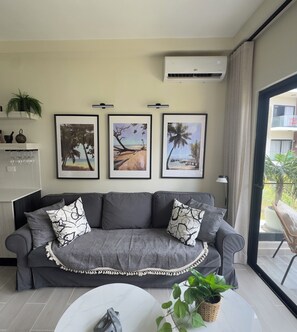 A modern living room with a grey sofa, three framed beach paintings, a white coffee table, and a potted plant. - Tropical Bliss apt, Beach, Golf, Dining,Gated community near downtown Punta Cana (Punta Cana)