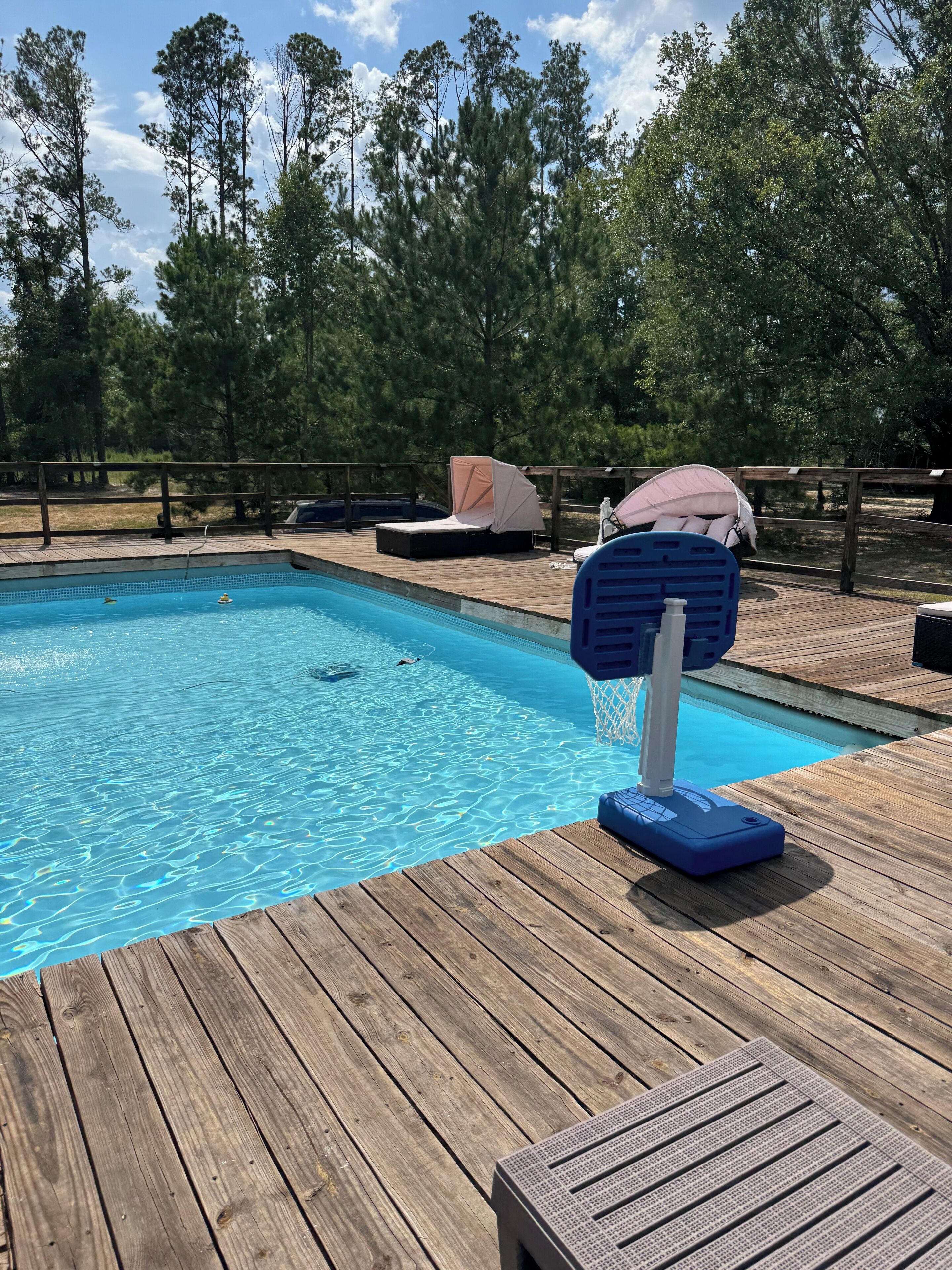 Una terraza de madera con piscina, sillas de descanso y un espacio de estar cubierto.