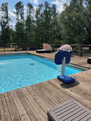 Um deck de madeira com piscina, espreguiçadeiras e uma área de estar coberta.