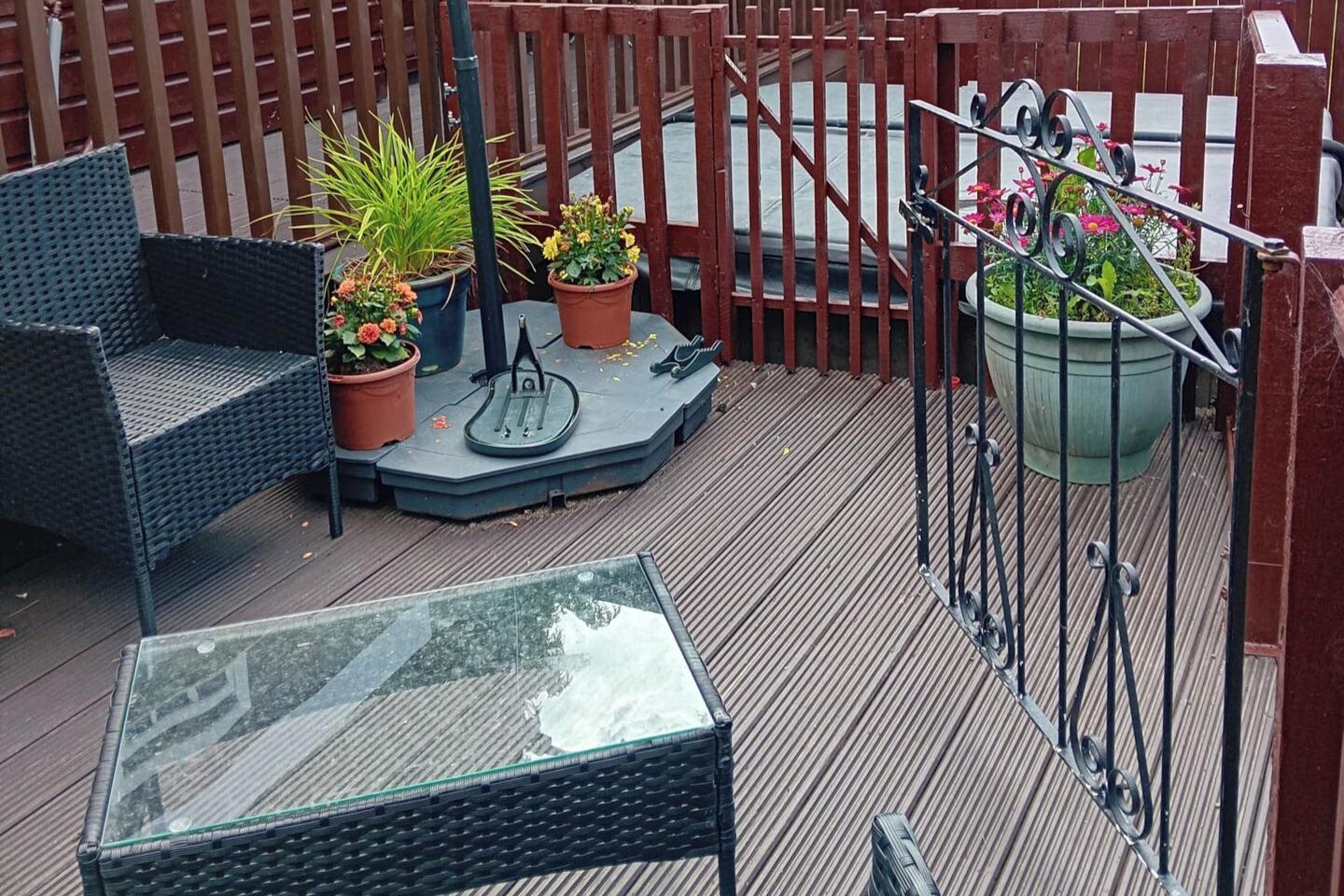 A deck with outdoor furniture, including a chair and a table, surrounded by potted plants and a metal gate.