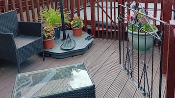 A deck with outdoor furniture, including a chair and a table, surrounded by potted plants and a metal gate.