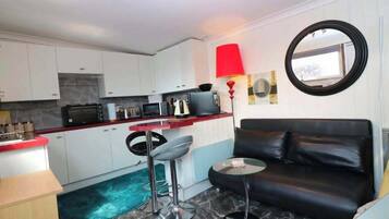 A compact living space with a kitchenette, a black leather sofa, a red floor lamp, and a round mirror on the wall.