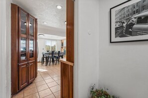 Un pasillo con un armario de madera, un comedor con sillas y una mesa, y un cuadro en la pared.