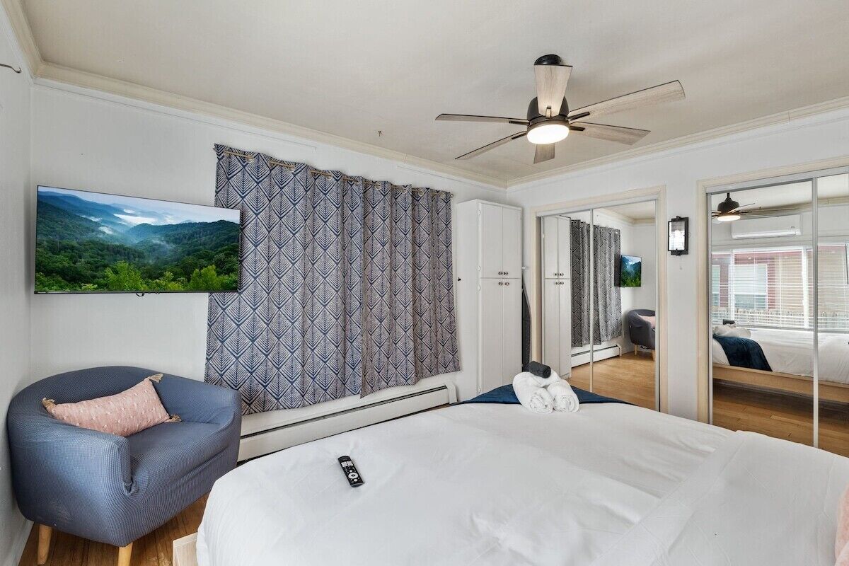 A hotel room with a bed, a chair, a television, and a ceiling fan.