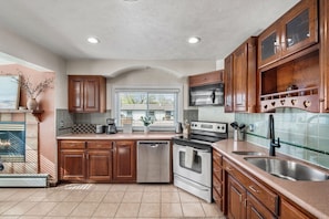 A kitchen with wooden cabinets, stainless steel appliances, and a large window. - Hot Tub Retreat - Near Downtown - Fenced Yard (Colorado Springs)